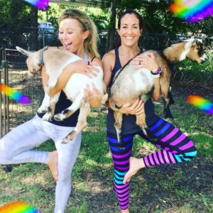 Two woman holding goats while doing yoga